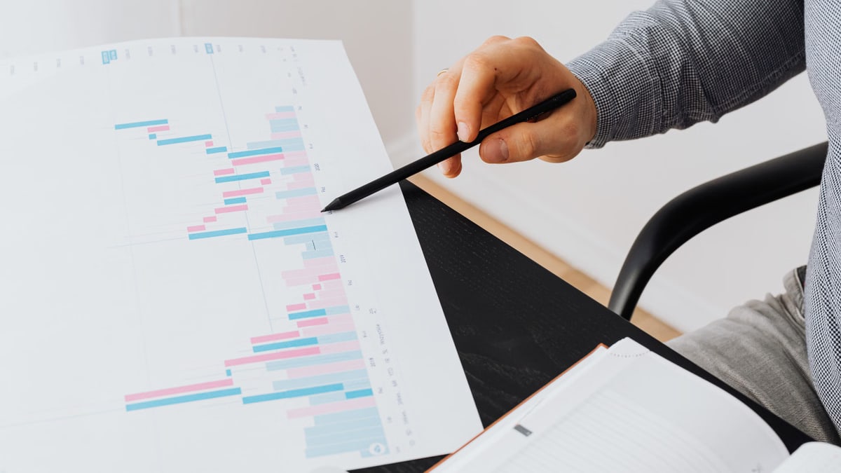 Close-up of a person analyzing a colorful graph chart with a pen in a modern office setting.